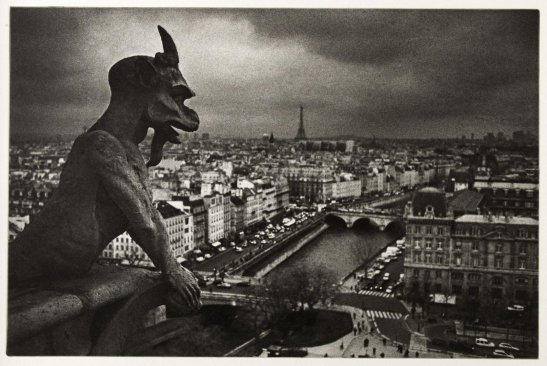 Photographie noir et blanc prise sur les hautre de la cathédrale avec au premier plan à gauche un gargouille à cornes surplombant Paris
